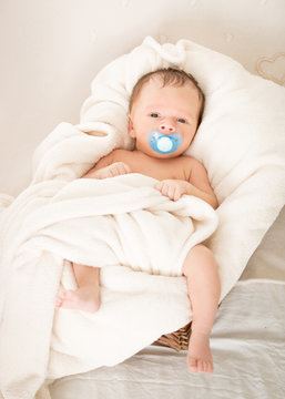 Cute baby with soother lying in wicker basket