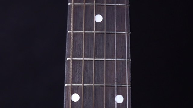 String of acoustic guitar, stands up, on black, close up, slow motion