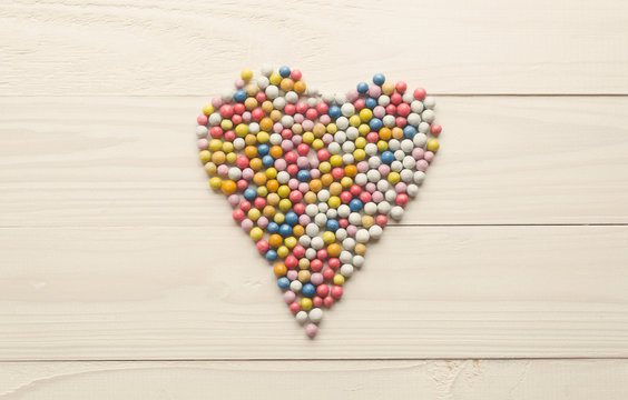 Toned image of colorful round candies lying in shape of heart on