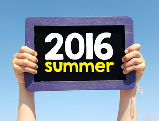 Hands holding blackboard with handwritten summer 2016 year, on blue sky background