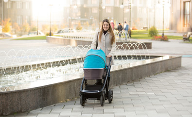 Happy mother with baby stroller walking on street near fountain