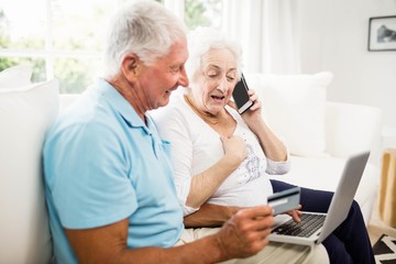 Smiling senior couple using laptop and smartphone - Powered by Adobe
