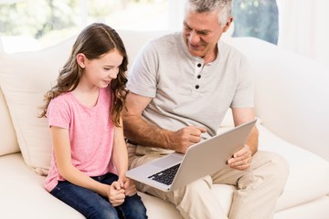 Smiling grandfather and granddaughter using laptop