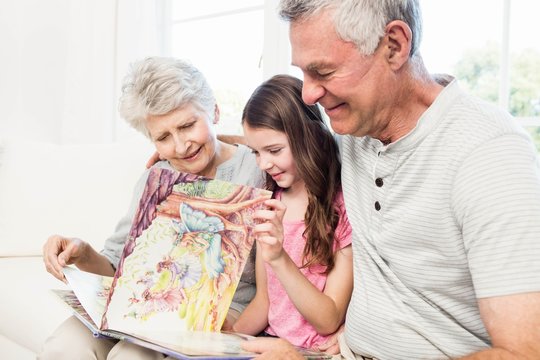 Happy Grandparents With Granddaughter Reading A Book