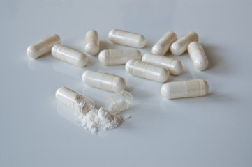 White medicine capsules with probiotic powder inside, one capsule open.
