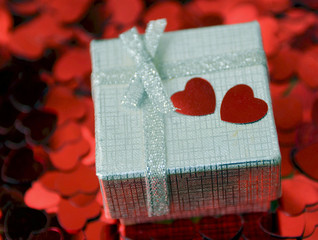 Valentines Day gift in silver box on decorative hearts confetti background.