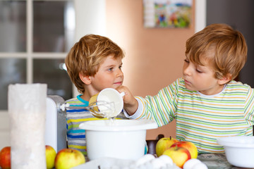 Two little kid boys baking apple cake indoors