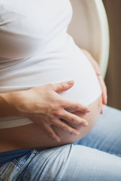 Pregnant woman holding belly with hands closeup