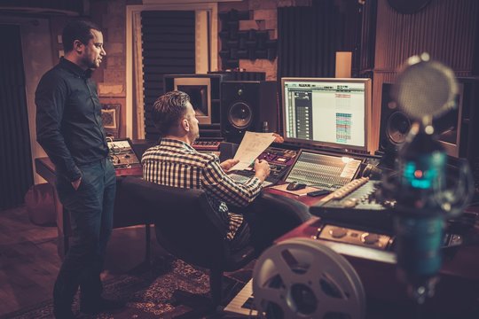 Sound engineer and producer working together at mixing panel in the boutique recording studio.