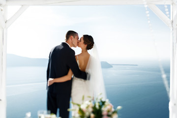 Newlywed husband and wife kissing at terrace looking at sea in S