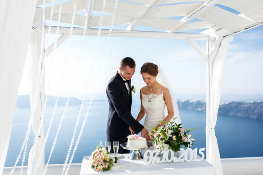 Bride and groom carving delicious white wedding cake sea backgro