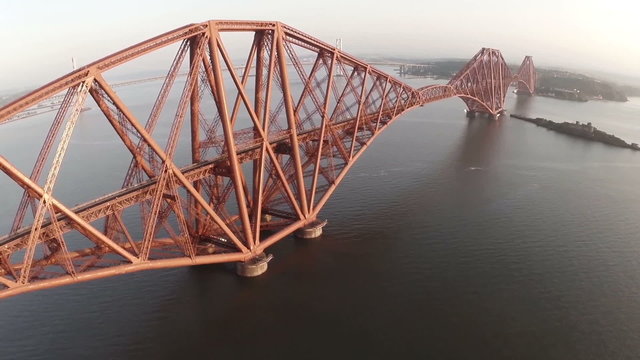 Aerial shot revealing the Forth Rail Bridge outside Edinburgh during sunrise on a calm summer morning
