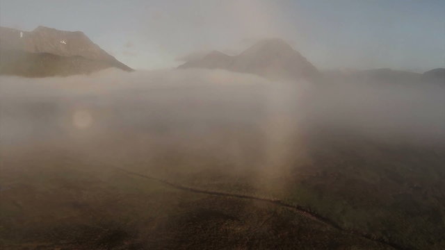 Aerial shot through cloud inversion revealing buachaille etive mor mountain during sunrise 
