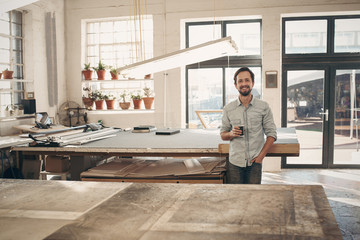Smiling entrepreneur standing in his workshop with coffee