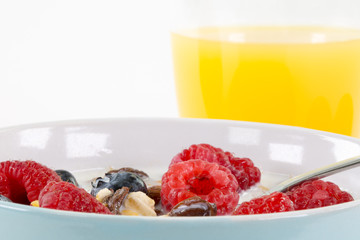 Macroaufnahme eines Früchtemüsli mit Himbeeeren in hellblauer Schale. Im Hintergrund ein glas...