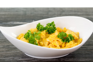 Eine Portion Rührei serviert in geschwungener weißer Schale, garniert mit Petersilie, auf dunkelgrauem Holztisch