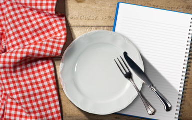 Notebook Plate and Cutlery / Empty plate with silver cutlery and open notebook for recipes or food menu on a wooden table with a red and white checkered tablecloth - Powered by Adobe