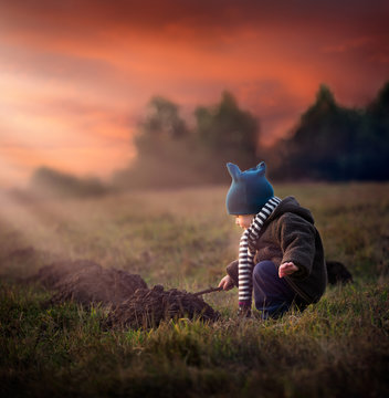 Small boy playing in outdoor at sunset. Boy digging in molehill with stick.