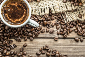 Cup of coffee and black coffee beans on wooden table