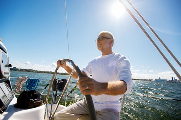 senior man at helm on boat or yacht sailing in sea