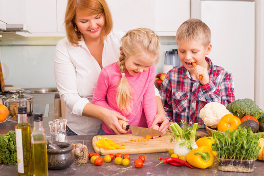 Mother teaching children how to cut vegetables 