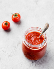 Tomato sauce in glass jar and cherry tomatoes on grey background Copy space