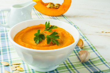 Pumpkin squash vegetable creamy soup with parsley in a white plate on white wooden background 