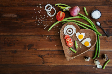 Vegetables and a plate with fried eggs in heart shape on wooden background overhead close up shoot