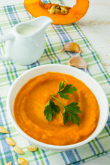 Pumpkin creamy soup with parsley in a white bowl on white wooden background, top view 
