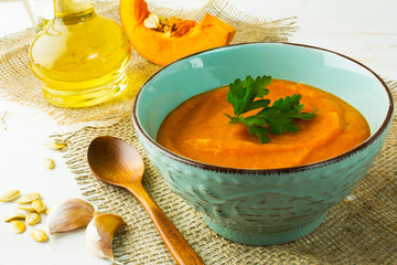 Roasted pumpkin cream soup with parsley in the turquoise cup on burlap, close up 