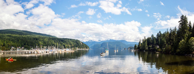 panoramic view of a bay in the middle of the mountains covered of a forest of pines with a small marina and mirror waters in british columbia of canada