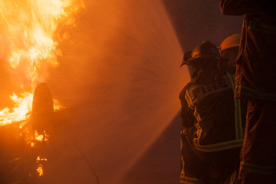 Silhouette of Firemen fighting a raging fire with huge flames of burning timber