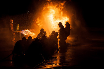 Silhouette of Firemen fighting a raging fire with huge flames of burning timber