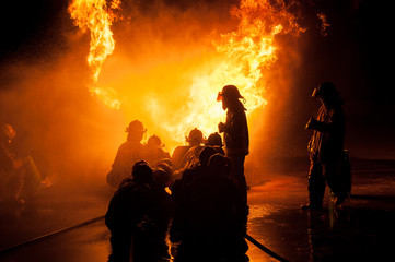 Fototapeta premium Silhouette of Firemen fighting a raging fire with huge flames of burning timber