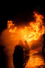 Obraz premium Silhouette of Firemen fighting a raging fire with huge flames of burning timber