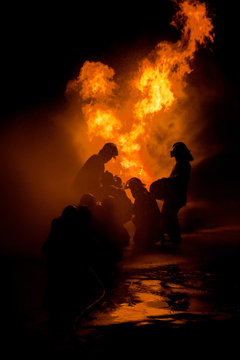 Silhouette of Firemen fighting a raging fire with huge flames of burning timber