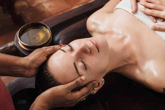 Ayurvedic face massage with oil on the wooden table