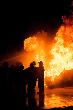 Silhouette of Firemen fighting a raging fire with huge flames of burning timber