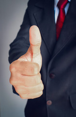 Businessman hand showing thumbs up on gray background.
