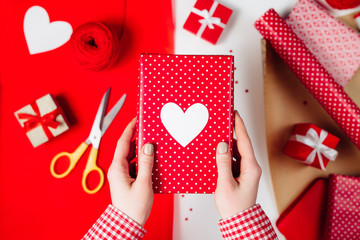Female hands are wrapping a valentines gift on red 