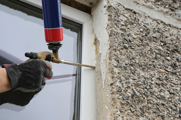 Worker's hand fix a window by  polyurethane foam - obrazy, fototapety, plakaty