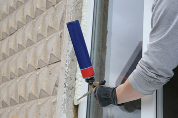 Worker's hand fix a window by  polyurethane foam - obrazy, fototapety, plakaty