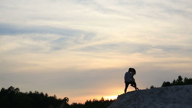 Sexy Brunnete Girl Kisses Her Boyfriend With Rose In Her Hand. Sunset And Woods On The Background