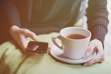 Young woman is drinking tea and using her smart phone