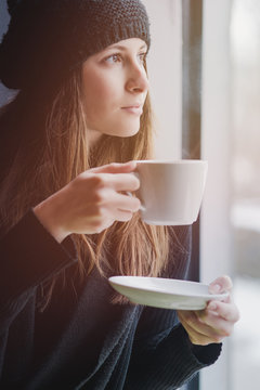 Young woman drinking tea in the morning while looking through the window