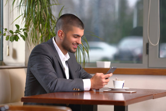 Smiling young businessman using his mobile phone while drinking coffee in a restaurant