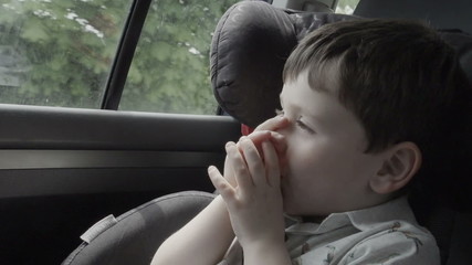 Closeup of a little boy sucking his thumb whilst traveling in a car