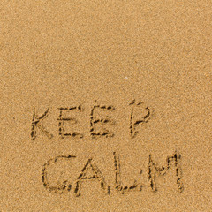 Keep calm - text written on sandy beach. Background, texture of the sand..