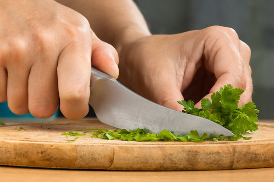 hands chopping leaves of parsley on the wooden cutting board