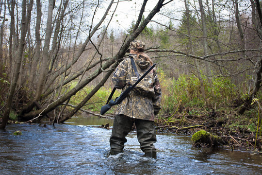 woman hunter in waders crossing small river in the forest